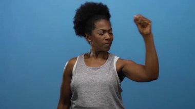 İzole edilmiş mavi arka planda kaslarını kasan kadın güç ve güç gösterisi yapıyor..