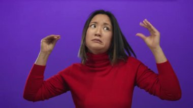 Kırmızı bir kazak giyen, duygularını ve iletişimini aktaran, canlı mor arka planda ellerini ifade eden bir kadın..