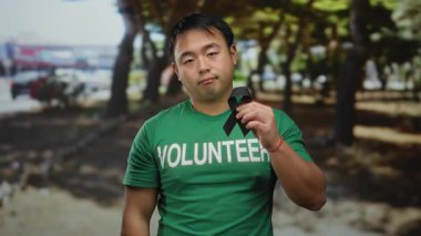 Yeşil gönüllü gömlekli genç adam park ortamında siyah kurdele tutuyor. Ağaçların ve bulanık çevrenin arka planına sahip kayıp ve anıları simgeliyor..