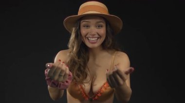 Stüdyoda, turuncu bikinili ve hasır şapkalı genç İspanyol kadın parmaklarını işaret ediyor..