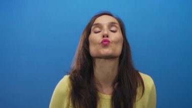 Genç İspanyol kadın dudakları stüdyo duvarında öpücük üflüyor ve eller parmaklarla kalp oluşturuyor; sevgi neşeyi seviyor.