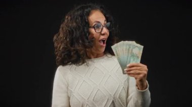 Uae 'de orta yaşlı bir kadın, elinde dirhem banknotları olan, siyah bir arkaplanı işaret eden, heyecan ve başarı gösteren,.