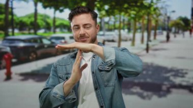 Sakallı genç adam güneşli bir şehir caddesinde mola veriyor..