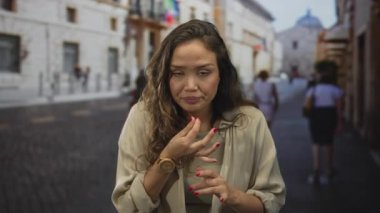 Kadın, tarihi bir binanın önündeki güneş ışığı parke taşı caddesinde burun hareketini çimdikliyor; iğrenme.