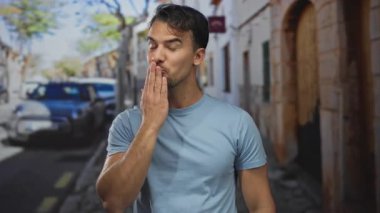 Mavi gömlekli genç adam, gülümsüyor ve güneşli şehir caddesinde öpüşüyor..