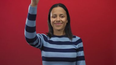 İzole edilmiş kırmızı arka plana başparmağıyla gülümseyen genç İspanyol kadın.