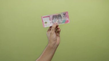 Sarı arka planda Endonezya parası tutan adam, izole edilmiş bir ortamda para gösteriyor..