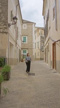 Tarihi binaları ve bulutlu gökyüzünün altında büyüleyici atmosferi olan Mallorca 'nın eski Akdeniz sokaklarında yürüyen bir kadın..