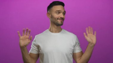 Beyaz tişörtlü, neşeli ifadeli ve stüdyo ortamında çekilen kolları açık pembe arka planda neşeli poz veren genç İspanyol bir adam..