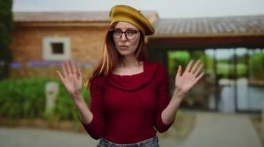 Bere takan ve gözlüklü bir kadın canlı bir şehir ortamında kızıl saçlarıyla kırsal bir binanın yanında kendine güvenen ve sıradan bir stil sergiliyor..