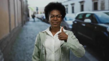 Dışarıda gülümseyen bir kadın, arka planda arabaları ve binaları olan şehir caddesinde olumlu bir jest yapıyor.