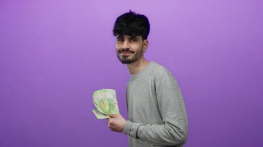 Canlı mor bir arka planda Rus rublesi tutan adam, kendine güvenen bir gülümsemeyle zenginlik ve ekonomik konsept sergiliyor..