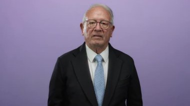 Takım elbiseli kıdemli bir adam, izole edilmiş mor bir arka plana karşı, düşünceli ve profesyonel bir ifade sergiliyor..