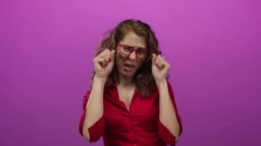 Dışlanmış pembe bir arka plan duvarından tiksinen bir kadın. Gözlüklü, yüz ifadeleriyle duygularını gösteren negatif duygular taşıyan bir kadın..