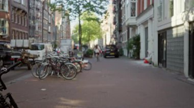 Bisikletler, Hollanda 'daki tipik şehir yaşamını gün ışığında canlı bir şehir ortamında sergileyen, odakları çözülmüş bir Amsterdam caddesi boyunca dizilmiş..