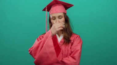 Yeşil arka planda duran pembe mezuniyet elbisesi içindeki kadın düşünceli ve düşünceli görünüyor. Genç bir öğrencinin başarıya ulaşma iç bakış açısını simgeliyor..