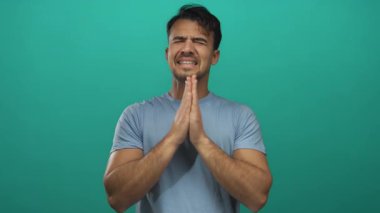 Genç adam canlı yeşil bir arka plana karşı dua ederek izole edilmiş bir stüdyo ortamında beklenti ve iyimserliği ifade ediyor.