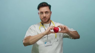Steteskoplu doktor gibi giyinmiş sakallı genç adam, kırmızı kalbi mavi duvarın üstünde tutuyor..