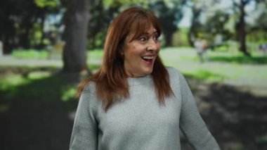 Güneşli bir günde yemyeşil bir parkta gülümseyen kıdemli İspanyol kadın neşe ve canlılık sergiliyor..