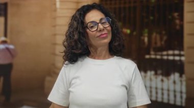 Orta yaşlı İspanyol kadın, tarihi eski kasaba caddesinde pazılarını göstermek için iki kolunu da esnetiyor..