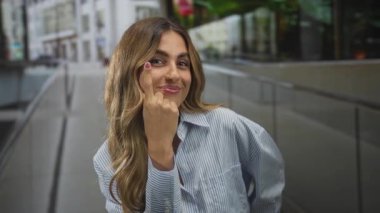 Meşgul şehir meydanında gözü işaret eden, gülümseyen sarışın kadın; dikkat farkındalığı özgüvene odaklanıyor.