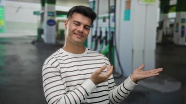 Genç adam bir benzin istasyonunu gösterip gülümsüyor, günlük kıyafetleriyle enerji ve güven taşıyor..