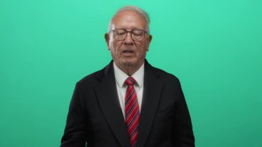 Takım elbiseli kıdemli işadamı, eli yürekli ve yükselmiş, sağlam yeşil bir geçmişe karşı duruyor, profesyonel bir ortamda söz veriyor ya da bağlılık gösteriyor..