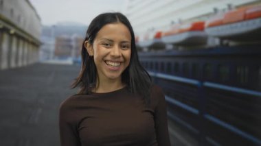 İspanyol bir kadın açık havada büyük bir teknenin arka planıyla sahil limanında öpüşürken neşeli bir ifade ve davetkar bir atmosfer yakalıyor..