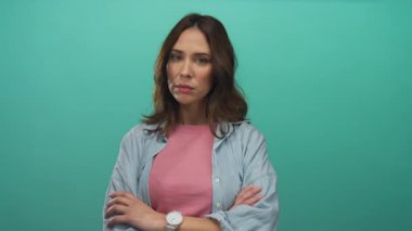 Kollarını kavuşturmuş genç İspanyol kadın yeşil arka plana karşı duruyor. Kendine güvenen ve tarzını belli eden günlük kıyafetler giyiyor..