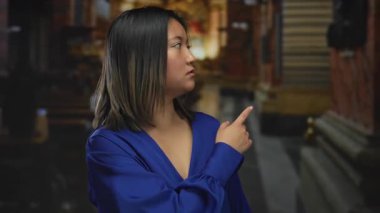 Mavi elbiseli genç Çinli bir kadın kilisenin içini işaret ediyor, bir iç mekandaki dekoratif mimariyi vurguluyor..