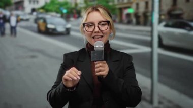 Şehir caddesinde mikrofon tutan genç kadın muhabir. Arka planda bulanık trafik ve yayalar var. Şehir yaşamının görüntülerini yakalıyorlar..