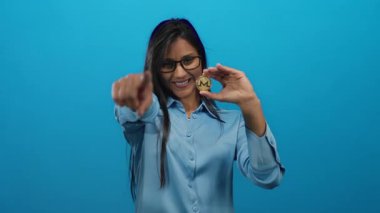 Monero sikkesi tutan kadın kameraya bakıyor, izole edilmiş mavi arka plan kripto para ve dijital para kavramlarını temsil ediyor..