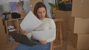 Kutularla çevrili bir dizüstü bilgisayarla çalışan ve yeni bir eve taşınıp rahat, modern bir iç mekâna yerleşen bir kadın..