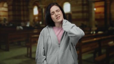 Boyun ağrısı çeken bir kadın loş bir Katolik kilisesinde, ahşap banklarla dikilirken..