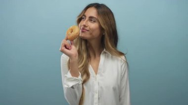 Beyaz bluzlu sarışın genç kadın stüdyo ortamında gözleri kapalı, burnunun yanında jöleli çörek tutuyor..