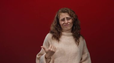 Kırmızı arka planda, gözlük ve süveter takan, isteksizlik ya da belirsizlik hissini aktaran, kuşkularını dile getiren bir kadın..