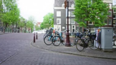 Arka planda bisiklet, kanal ve kadın ile Amsterdam caddesinin bulanık görüntüsü, Hollanda 'nın canlı, odaksız şehir manzarasını sergiliyor.