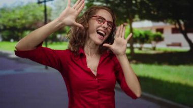 Güneş parkında gözlüklü, kırmızı tişörtlü bir kadın. Etrafı yeşilliklerle çevrili. Neşe ve boş zamanların somutlaştırıcısı..