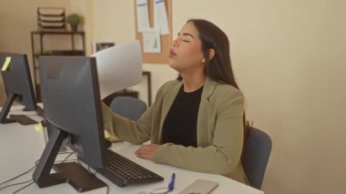 Ofiste masa başında çalışan bir kadın, profesyonel giyimli ve modern çalışma ortamı olan kapalı alandaki belgelere odaklanan bir bilgisayar kullanıyor..