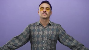 Gömleği desenli genç adam kollarını izole edilmiş mor arka plana karşı güvenli bir şekilde açıyor.