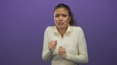 Beyaz elbiseli kadın, canlı mor bir arkaplan karşısında korkusunu dile getiriyor, soyutlanmış, duygusal ve gergin bir an sergiliyor..