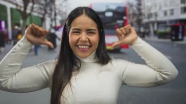 Genç Latin asıllı, açık havada mutlu ve gülümseyen birini işaret ederken kadın başparmağını tutuyor..