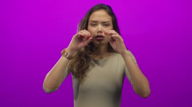 Genç İspanyol kadın pembe stüdyoda gözlerini nazikçe ovalıyor. Günlük bol bej gömlek giyiyor. Yorgunluk giderici..