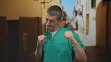 Yeşil doktor üniformalı beyaz adam güneşli caddede zaferi kutluyor. Yumrukları havada, mutluluğu ve başarıyı yansıtıyor..