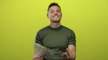 Hispanik adamın elinde dolar hayranı canlı sarı bir arka plana karşı güler. Karizma ve finansal başarı yayarken aynı zamanda neşeli bir kalp hareketi yapar..