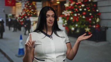 Genç bir kadın, şenlikli bir şehir caddesinde, gösterişli bir tatil süslemeleri ve düşünceli bir ifadeyle el kol hareketi yapmaz..