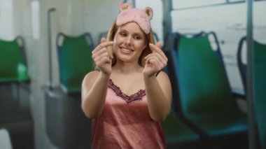 Pembe gecelikli genç bir kadın geceleri otobüste ellerini kullanarak kalp hareketi yapıyor. Hoş bir uyku maskesi takıyor. Eşsiz bir seyahat ortamında neşeli ve samimi titreşimler yayıyor..