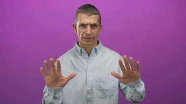 Çizgili tişörtlü beyaz adam, canlı pembe arka plana karşı sakin bir jest yapıyor. Etkileyici el hareketleri ve odaklanmış davranışlar yoluyla sükunet duygusu yayıyor..