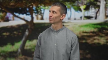 Güneşli bir park ortamında, bulanık yeşillik ve ağaçlarla duygularını ifade eden bir adam, sıradan bir öğleden sonra atmosferini yakalıyor..