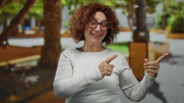 Parkta, yeşil yeşil bir ortamda gülümseyen, sıradan beyaz kıyafetler ve gözlük takan, neşe ve mutluluk saçan bir kadın..